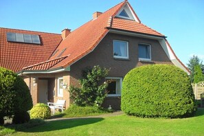 Ein zweigeschossiges Haus mit rotem Ziegeldach, einer Veranda und einem gepflegten Garten.