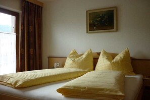 Ein Doppelbett mit gelber Bettwäsche, ein Gemälde an der Wand und ein Fenster mit Vorhängen.