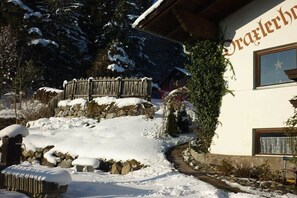 Eine verschneite Außenanlage mit Holzpforte, Steinmauer und einem Gebäude mit Schild.