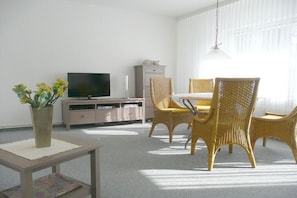 Ein Wohnzimmer mit Fernseher, Korbstühlen, einem kleinen Tisch und einem Schrank.