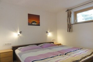 Ein Schlafzimmer mit einem Bett, zwei Nachttischlampen, einem Nachttisch, einem Fenster mit Vorhängen und einem Wandbild.