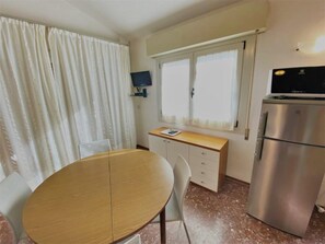 Eine kleine Küche mit Holztisch, Stühlen, einem Kühlschrank und einem Fenster mit Vorhängen.