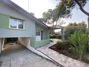 Ein modernes Haus mit Flachdach, überdachter Veranda und einem kleinen Garten.