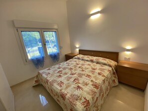 Ein Schlafzimmer mit einem Bett, zwei Nachttischen, einem Fenster mit Vorhängen und Wandleuchten.