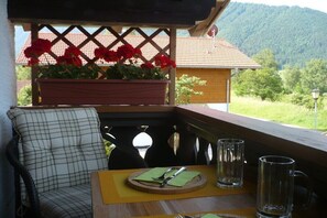 Eine hölzerne Bank mit kariertem Sitzkissen, ein Tisch mit Unterlage, ein Teller mit Besteck und zwei Gläser.