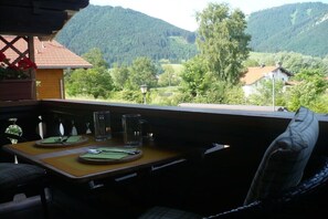 Un balcón con una mesa dispuesta para dos personas, con vistas a un paisaje montañoso.