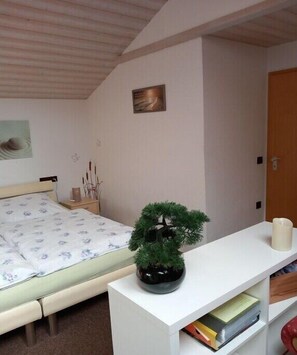 Ein Schlafzimmer mit einem Bett, einer kleinen Topfpflanze, einem Nachttisch, einem an der Wand befestigten Regal und einer Tür.