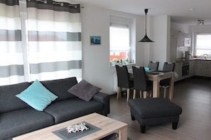 Ein modernes Wohnzimmer mit einer Couch, einem Hocker und einem Essbereich mit Stühlen und einem Tisch.