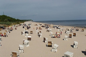 Ein Strand mit vielen weißen Liegen und Sonnenschirmen, feinem Sand und einem klaren Himmel.