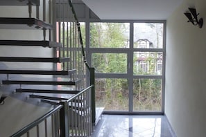 Ein modernes Interieur mit einer Treppe, großen Fenstern und Blick auf ein Gebäude sowie Bäume.