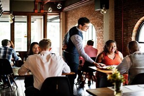 Ein Restaurant mit Backsteinwänden, großen Fenstern und einem Kellner, der ein Tisch bedient.