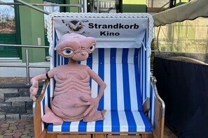 Eine pinkfarbene aufblasbare Figur in einem Strandkorb mit einem gestreiften Verdeck, das 'Strandkorb Kino' beschriftet.