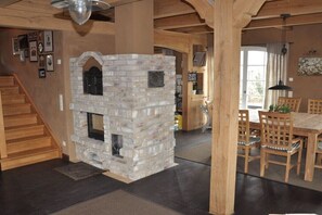 Ein rustikales Interieur mit Kamin aus Stein, einer Holztreppe und einem Essbereich mit Holzmöbeln.