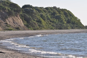 Ein Strand mit Wellen, einem sandigen Ufer und einer bewaldeten Hügelkette im Hintergrund.