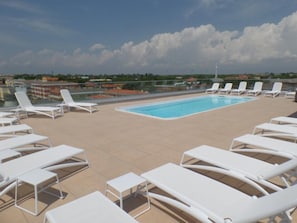 Ein Pool auf dem Dach mit weißen Liegestühlen und freiem Blick auf die umliegenden Gebäude.