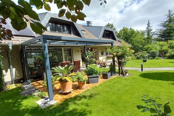 Une maison dotée d’un patio couvert, d’une façade en briques et d’un jardin bien entretenu.