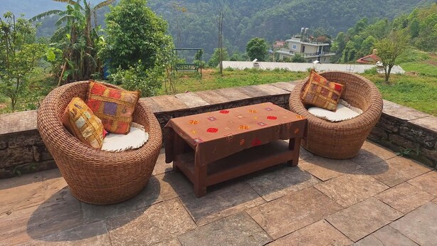 Un espacio de estar exterior de ratán con cojines, una mesa de madera y vistas a un paisaje montañoso.