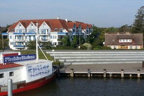 Ein an einem Steg liegendes Boot mit einem Schild, auf dem 'Fischbrücken' steht, und im Hintergrund ein Gebäude mit rotem Dach und blauen Fenstern.