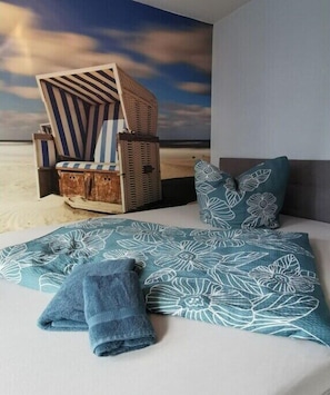 Ein Bett mit einer blumigen Tagesdecke, ein blaues Handtuch und ein gestreifter Stuhl mit einem Korb.