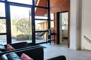 Ein modernes Wohnzimmer mit einem großen Glasfenster, das in einen Außenbereich führt, einer schwarzen Ledersofa und einem kleinen Tisch mit einer Pflanze.