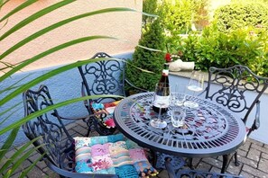 A round metal table with a bottle and glasses, surrounded by metal chairs with colorful cushions. - Holiday apartment Nonnenbergblick (Bad Tabarz)