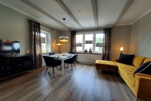 A modern living room with a sofa, dining table, and TV. - Holiday apartment Nonnenbergblick (Bad Tabarz)