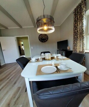 A dining area with a table set for four, a clock on the wall, and a television in the background. - Holiday apartment Nonnenbergblick (Bad Tabarz)
