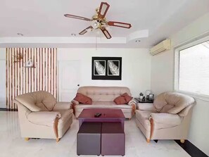 Ein modernes Wohnzimmer mit einer Sofagarnitur, zwei Sesseln, einem Couchtisch, einem Deckenventilator und zwei gerahmten Bildern an der Wand.