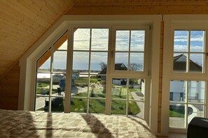 Ein Zimmer mit schrägem Dach, großen Fenstern und Blick auf eine Wohngegend.