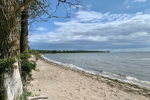Ein Strand mit sandigem Ufer, einem von Bäumen gesäumten Pfad und einer entfernten Küstenlinie.