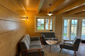 Ein Holzinterieur mit einer Couch, zwei Sesseln, einem kleinen Tisch und einem Fenster mit Blick.