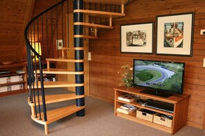 Eine Wendeltreppe aus Holz, ein Fernseher auf einem Holztisch und gerahmte Bilder an der Wand.