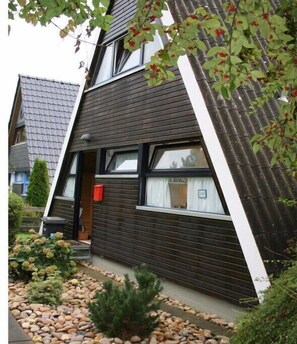 Ein modernes Haus mit Satteldach, einer Haustür und einem kleinen Garten mit Steinen und Pflanzen.