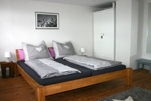 A double bed with a wooden frame, two bedside tables with lamps, a white wardrobe, and a framed picture on the wall. - Holiday home with 2 bedrooms (Neuhausen)
