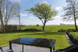 Eine Terrasse mit einem Glastisch, umgeben von einem gepflegten Rasen und Bäumen.