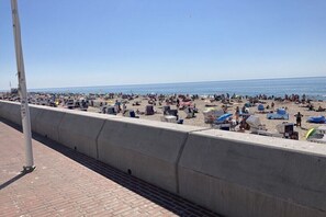 Ein Strand mit einer Betonbarriere, Personen und Sonnenschirmen.