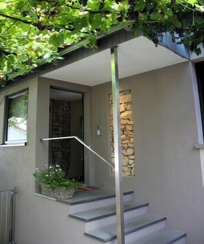 Ein modernes Gebäude mit einer Wand aus Stein, einer Metalltreppe und einem kleinen Balkon mit Pflanzen.