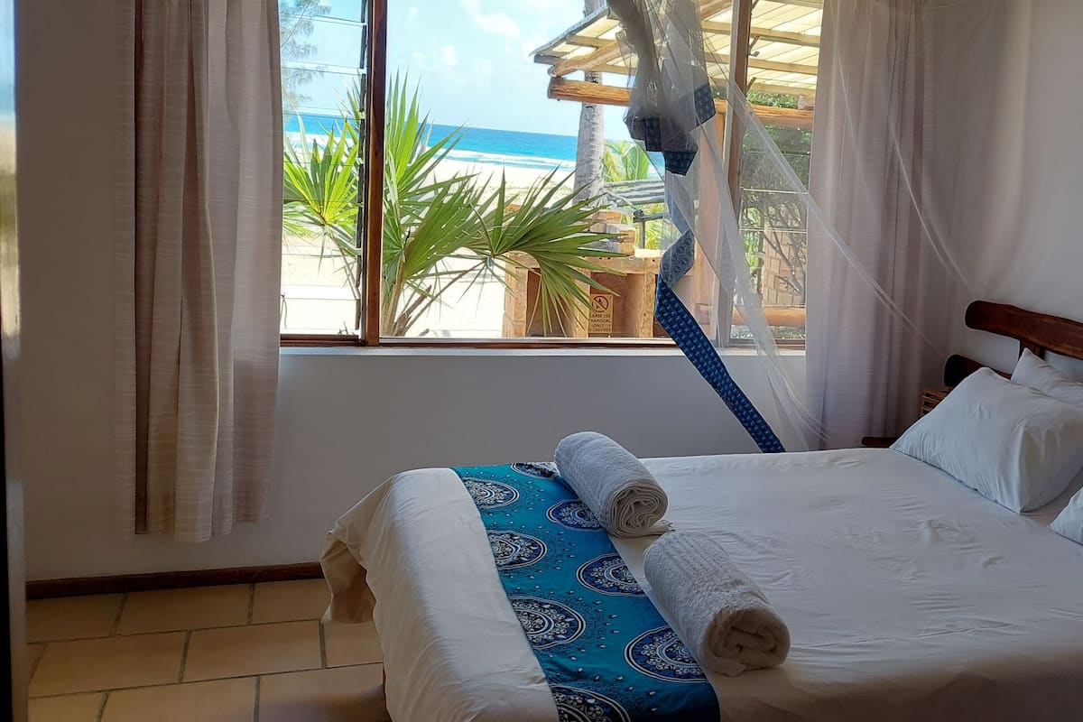 A bed with white linens, a blue patterned bedspread, and a rolled towel.