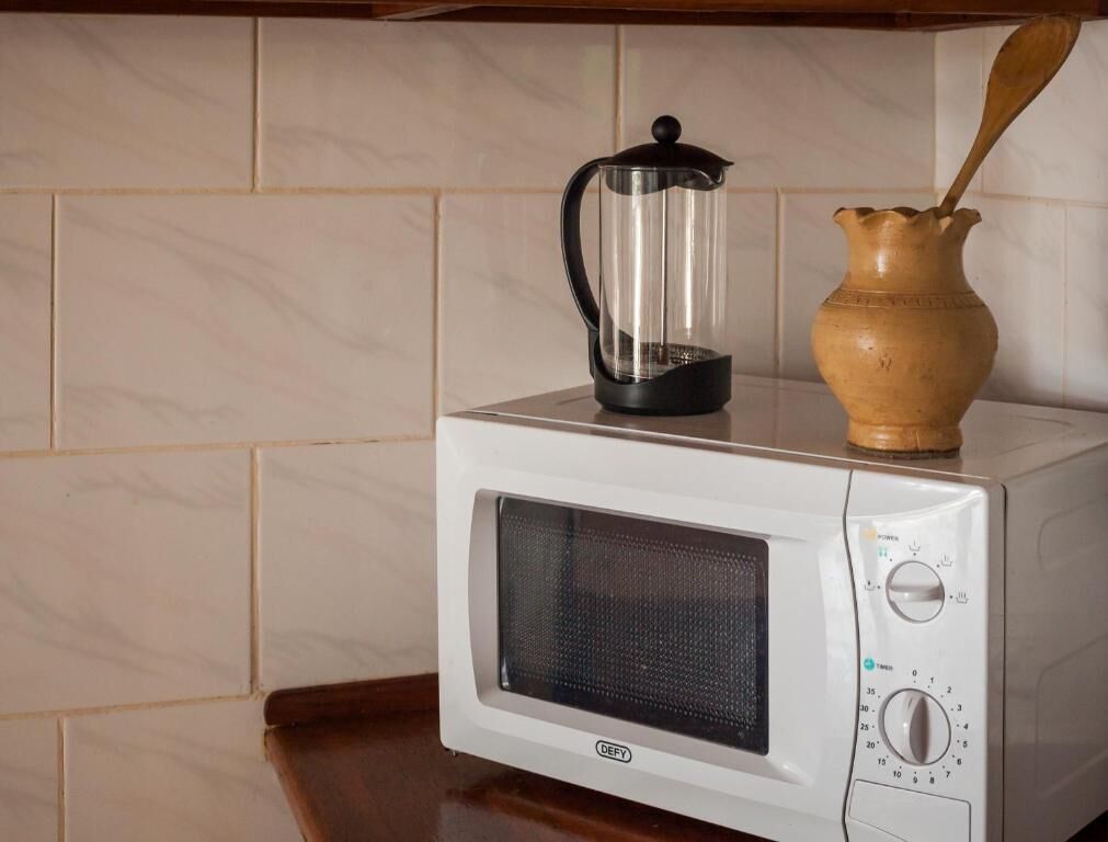 Un microondas con una cafetera transparente encima y una jarra de madera al lado.