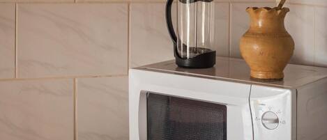 Un microondas con una cafetera transparente encima y una jarra de madera al lado.