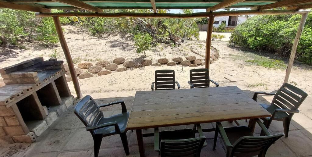 Terrassa exterior amb taula i cadires de fusta, una barbacoa i una paret de pedra.