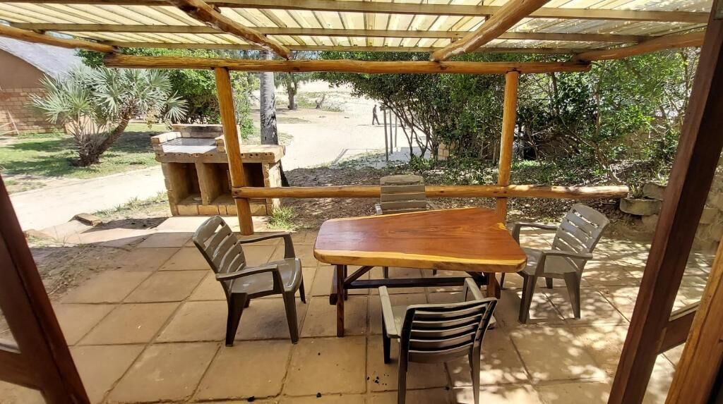Un patio al aire libre con una mesa y sillas de madera, un banco de piedra y una estructura de pérgola.