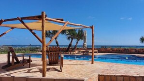 Un espace piscine agrémenté d’une pergola en bois, de chaises longues et offrant une vue sur l’océan.