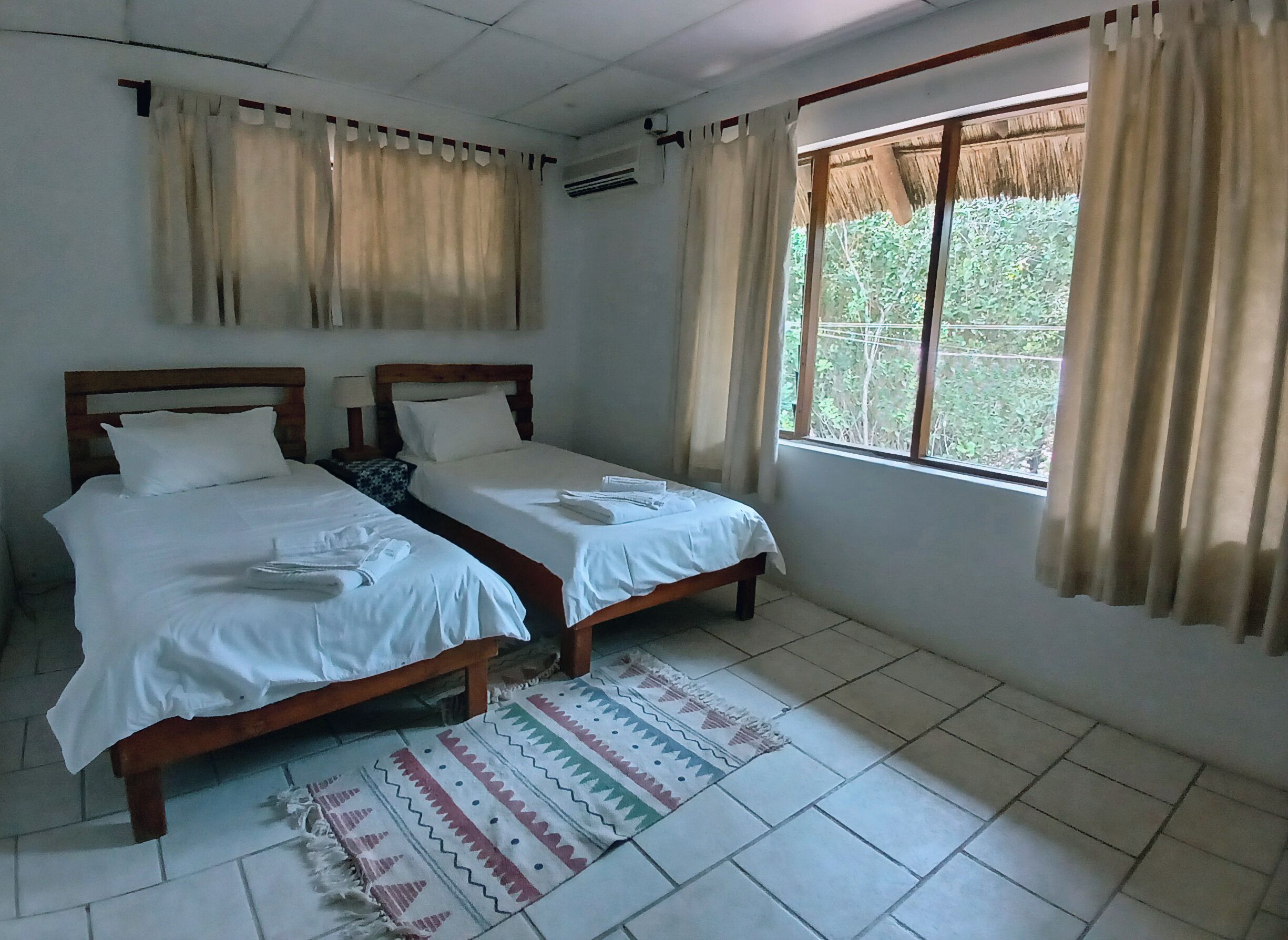 Une chambre avec deux lits, une fenêtre avec des rideaux, un tapis à motifs et un ventilateur de plafond.