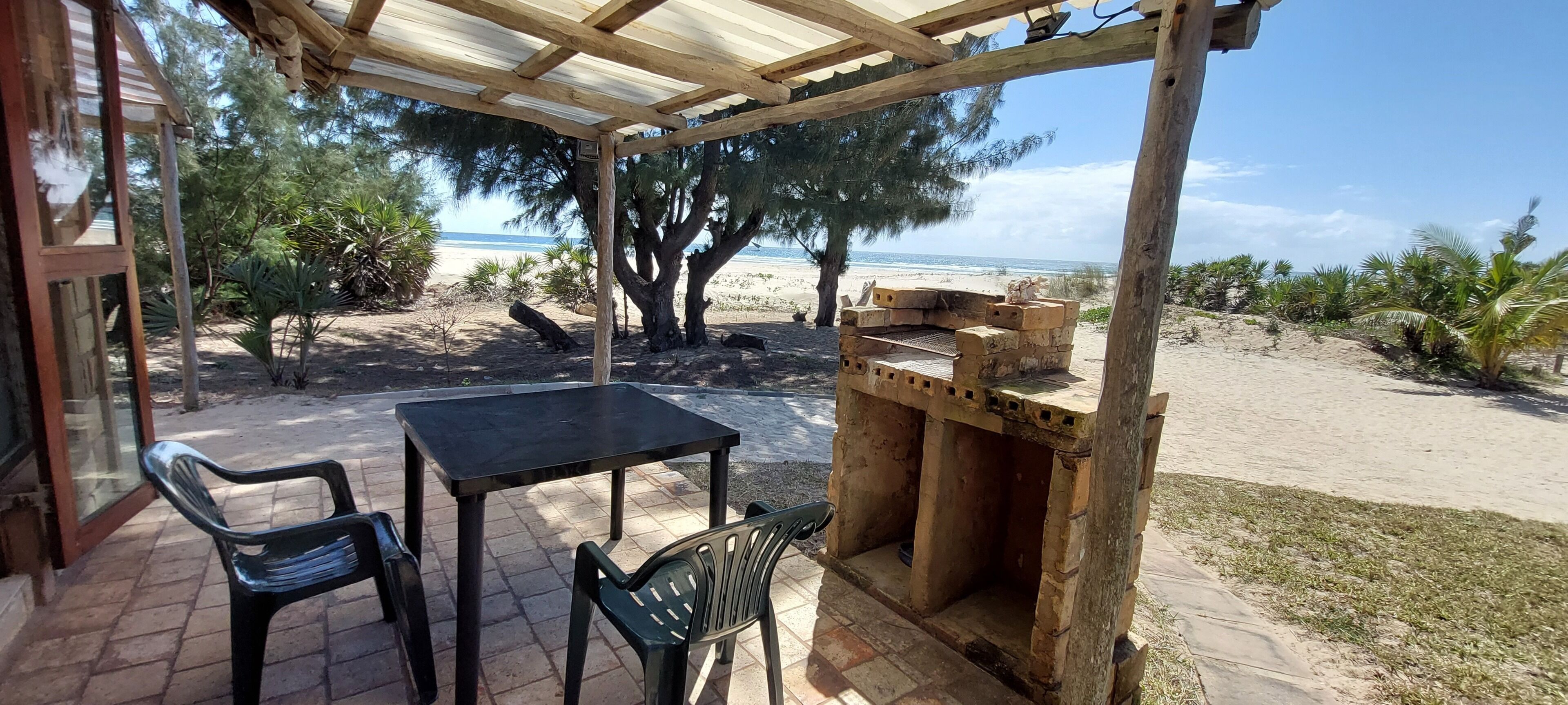 A covered patio with a table and chairs, a brick grill, and a view of the beach and ocean.