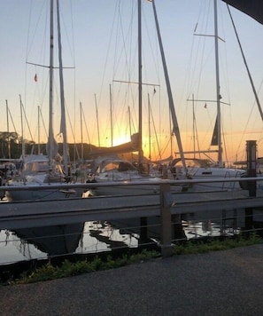 Ein Yachthafen mit mehreren Segelbooten, eine ruhige Wasseroberfläche und ein Sonnenuntergang im Hintergrund.