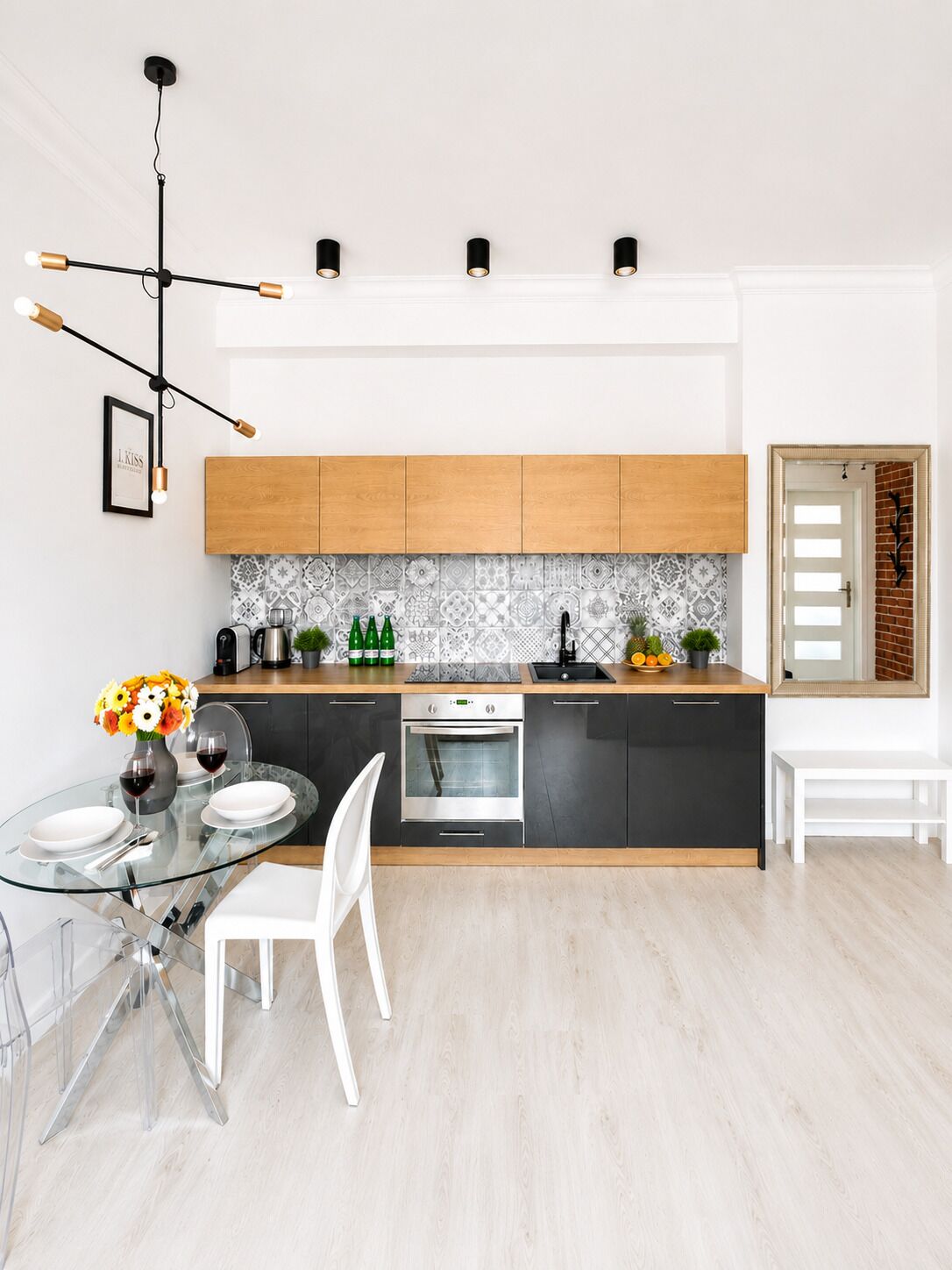 A modern kitchen with a glass dining table, white chairs, a built-in oven, and a wooden countertop.