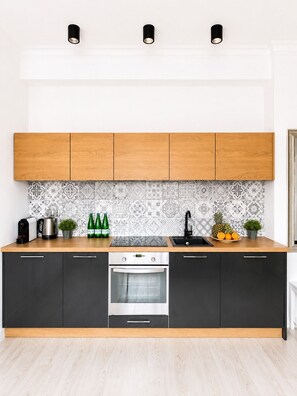 Een moderne keuken met houten kastjes, een oven van roestvrij staal, een koffiezetapparaat en een betegelde spatwand.