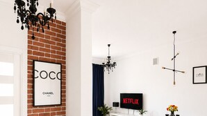 A modern living room with a brick accent wall, a black and white tiled floor, a sofa, a bench, a dining area with a table and chairs, and a TV displaying 'NETFLIX'. - Lumina Cozy Apartment in Warsaw Centre (Warsaw)