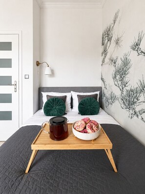 Un dormitorio con una cama, una bandeja con una taza y donas, y una pared con un mural de plantas.
